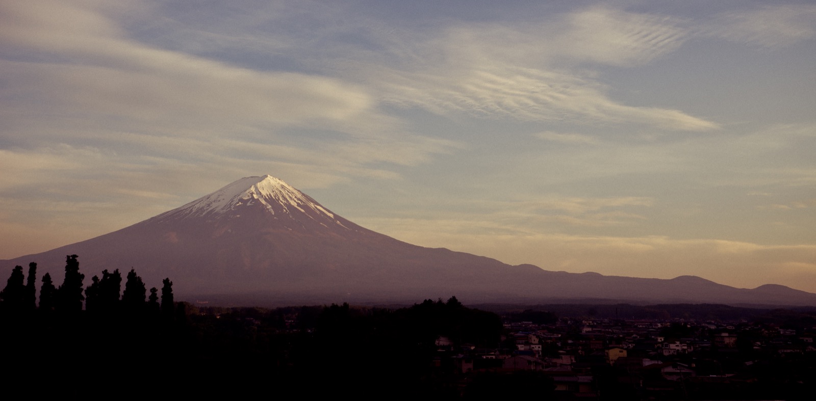 Mount Fuji rises above the darkening landscape at dusk.